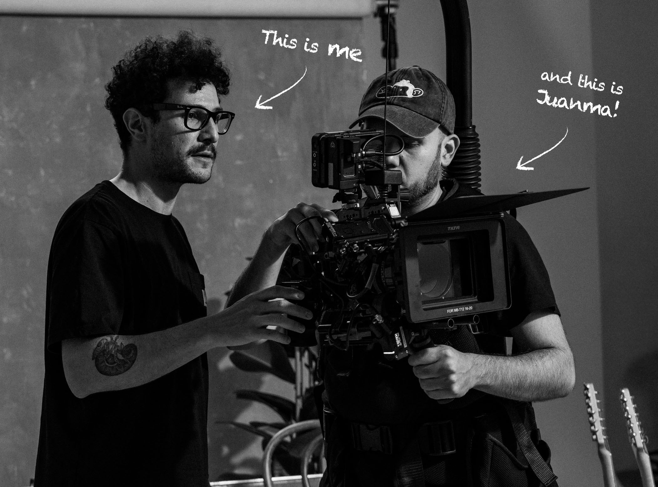 Dos personas de pie detrás de una cámara de cine profesional; un texto escrito a mano señala a cada una diciendo ¡Este soy yo y este es Juanna!.