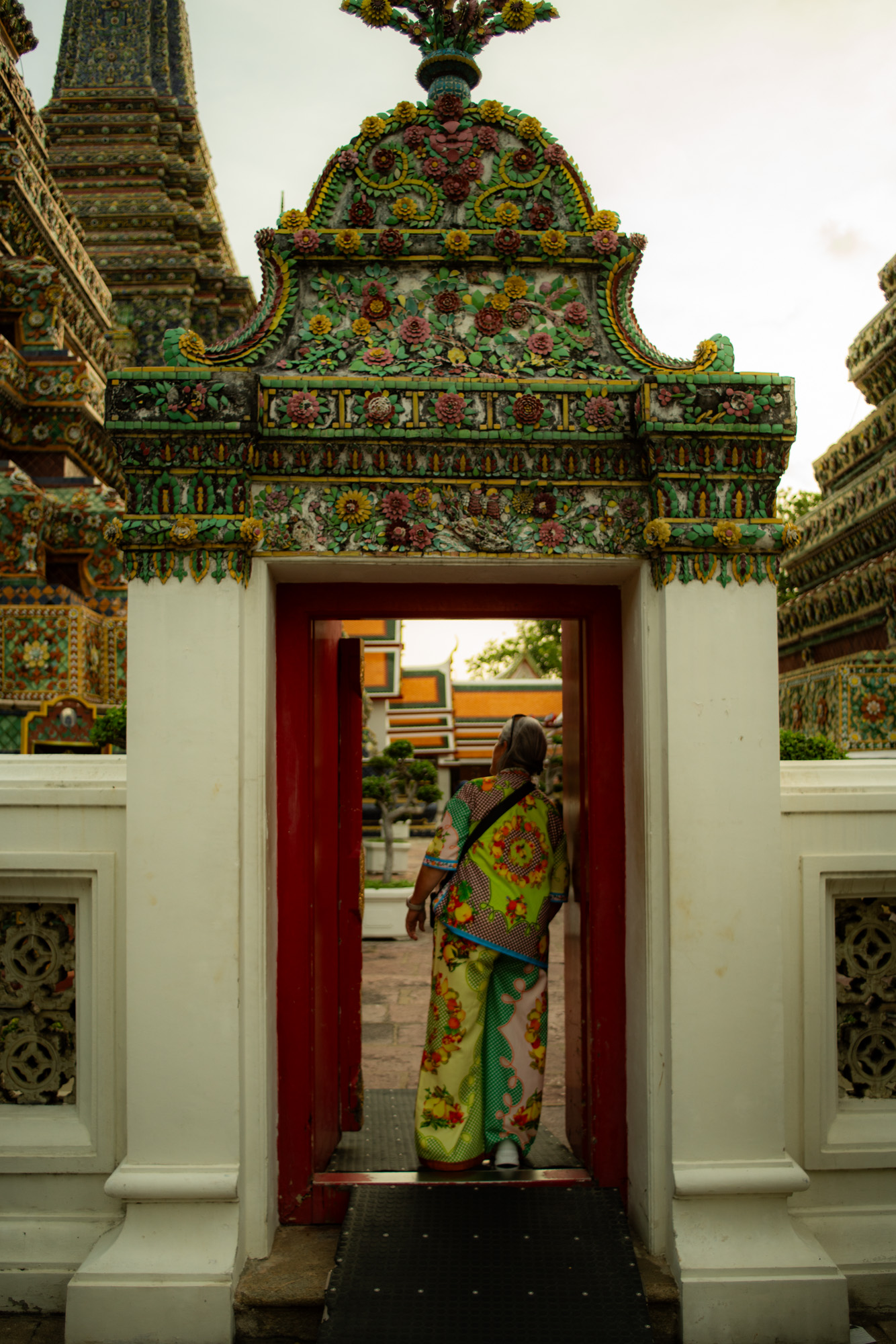 Una persona vestida con ropas de colores se encuentra en la puerta de un templo enmarcado por una arquitectura tradicional ornamentada.